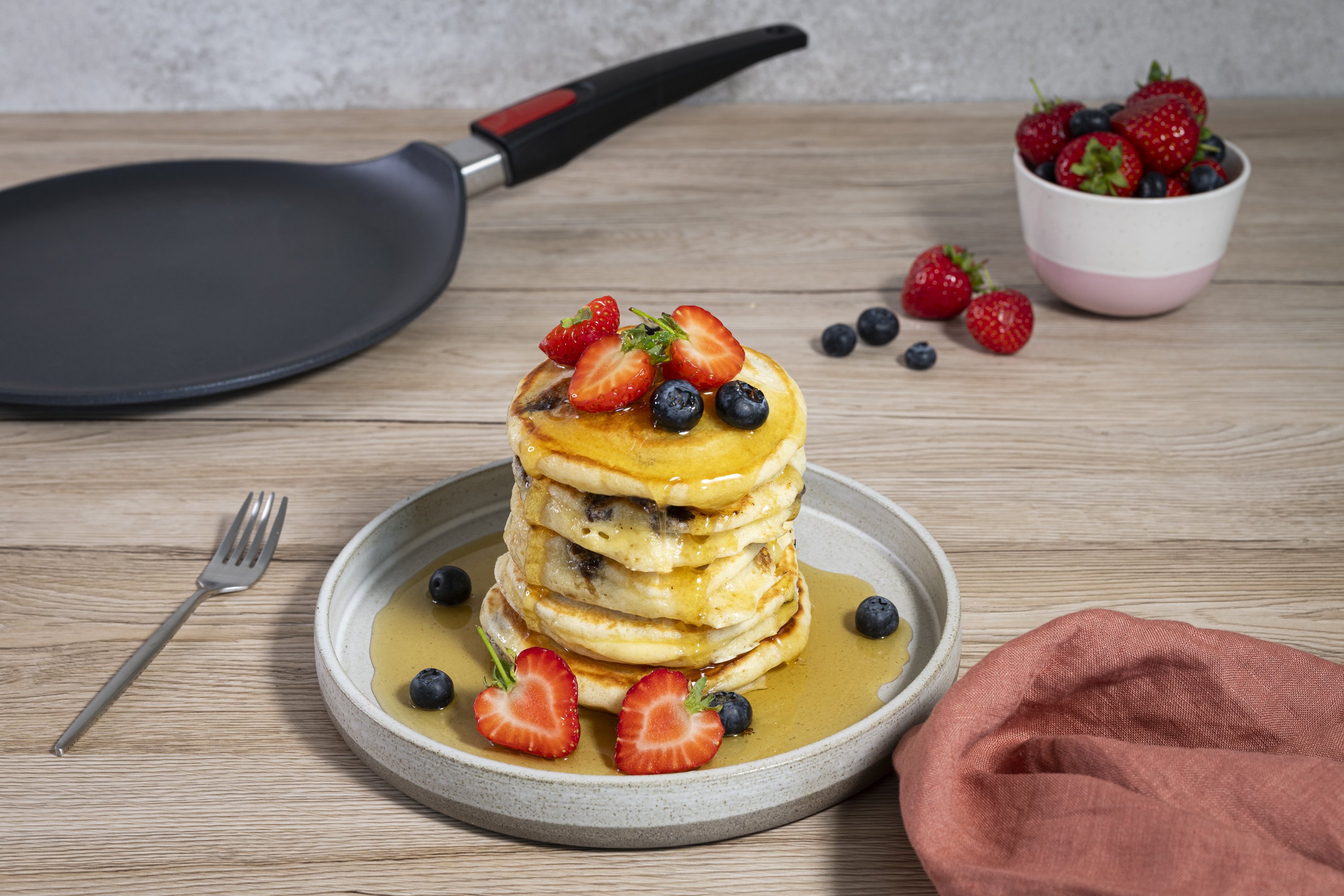 Auf einem Teller liegt ein Stapel garnierte American Pancakes. Im Hintergrund steht eine Diamond Lite Crêpepfanne.