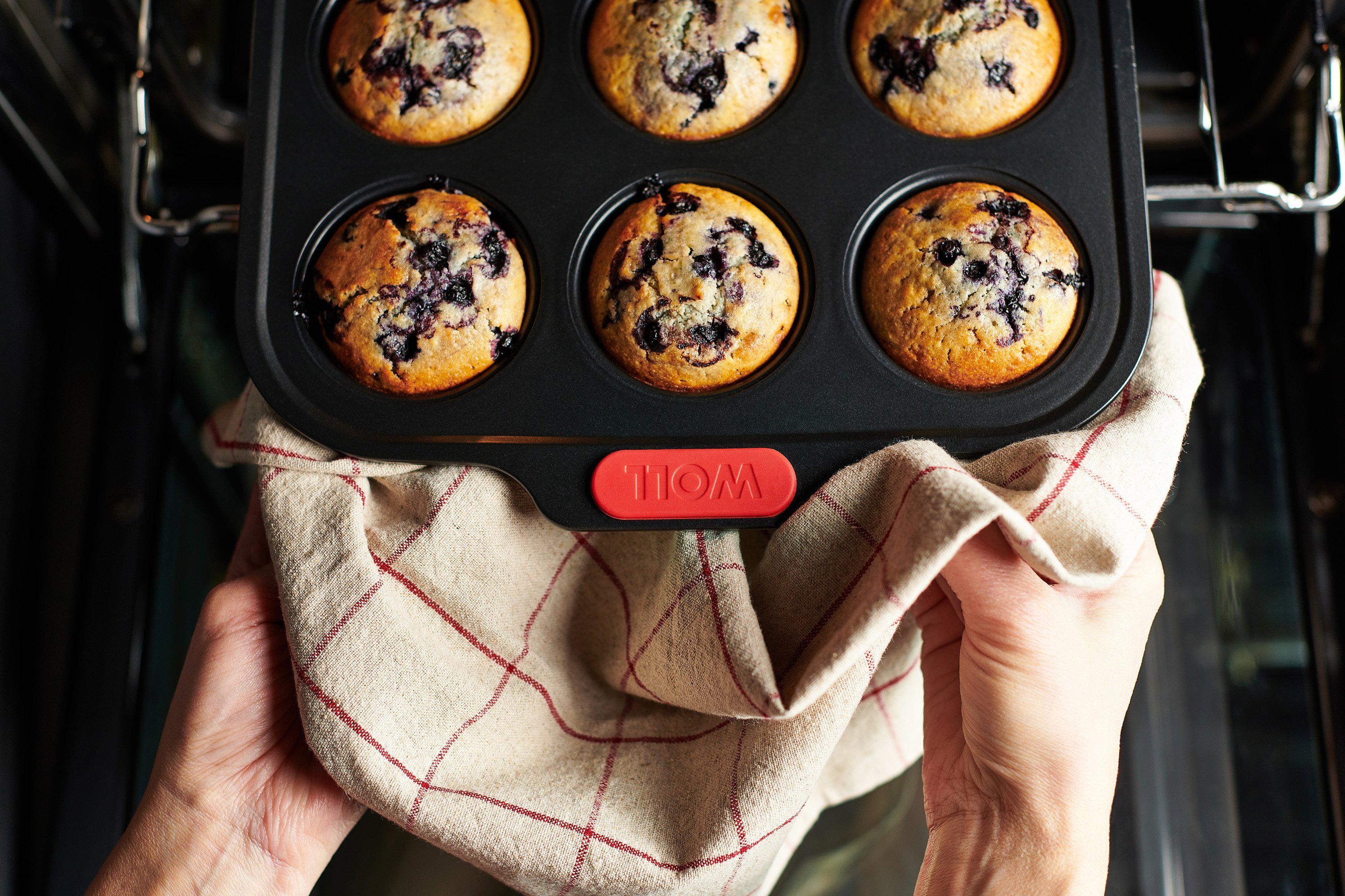 Eine rechteckige Let's bake! Muffinform enthält frisch gebackene Blaubeermuffins. Sie wird mit einem Küchentuch aus dem Backofen genommen.