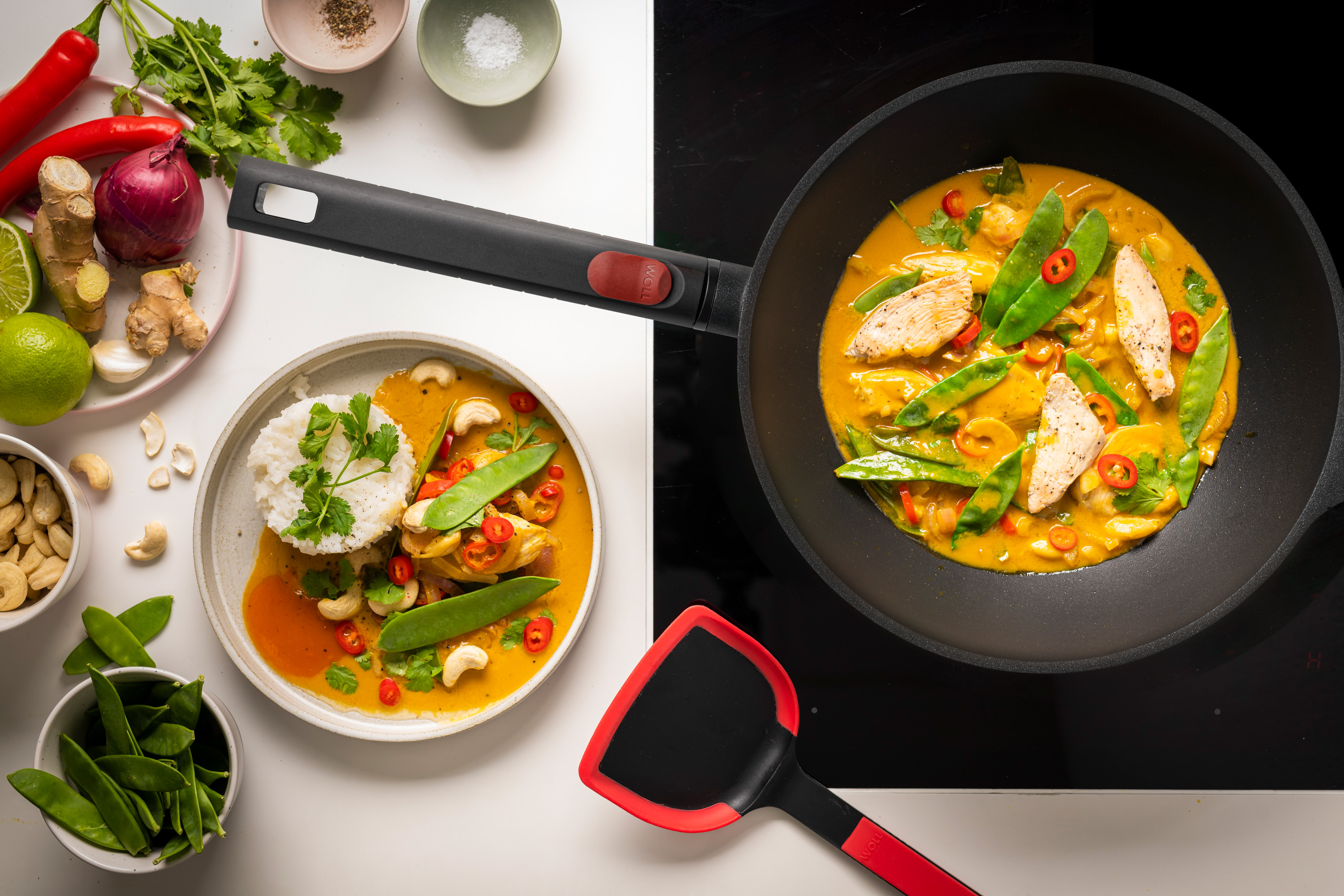 Logic XR Wok-Set, 3-tlg., Ø 24 cm Auf dem Herd steht eine runde Logic XR Wok- und Rührpfanne, in der Curryhähnchen zubereitet wird.
