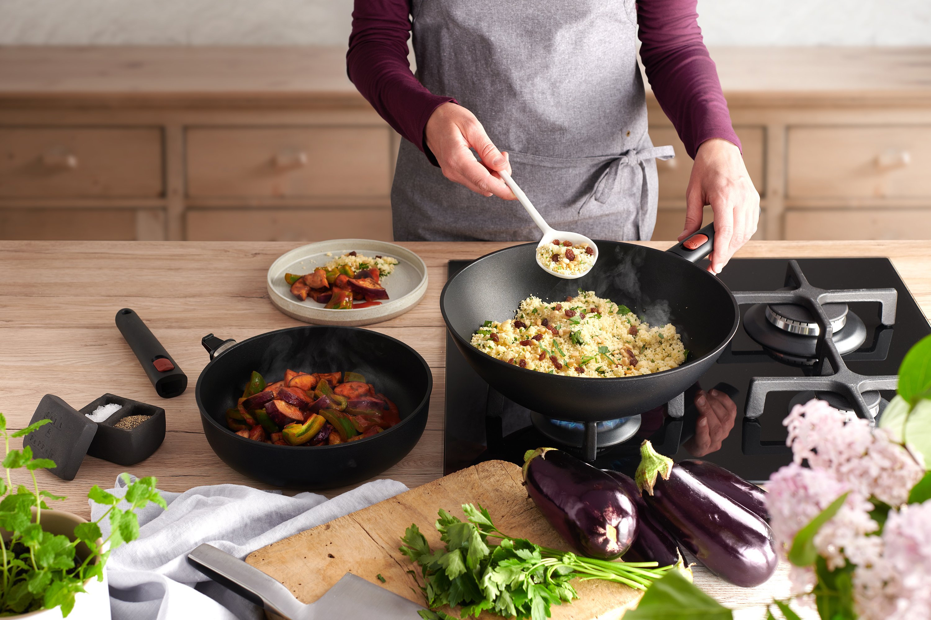 In einem runden Eco Lite Wok wird Couscous Salat zubereitet. Daneben steht eine weitere Eco Lite Pfanne mit Gemüse.